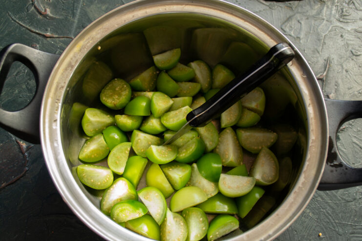 Step 2: Quartering the physalis berries for the jam. A pile of quartered green physalis berries on a cutting board.