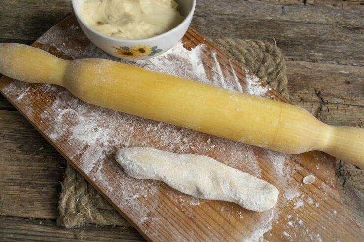 Shaping the dough into logs for easy portioning of individual vareniki. Vareniki dough divided into several long logs on a floured wooden board.
