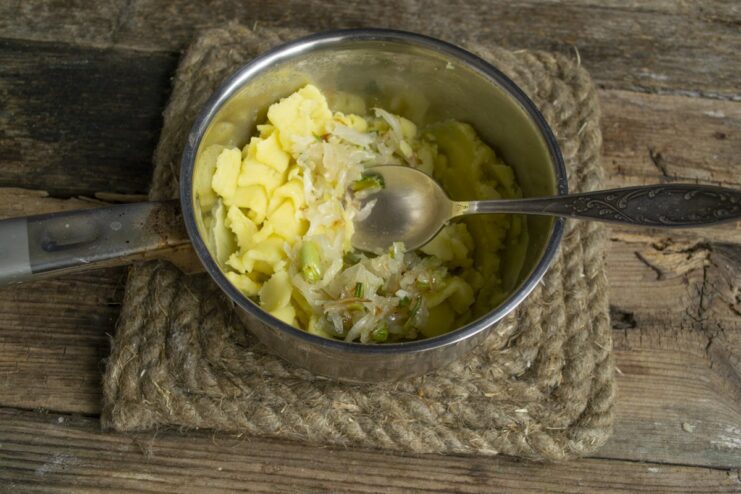 Adding flavor: Sautéed onions are mixed into the potato filling. Sautéed onions and green onions being added to a pot of mashed potatoes.