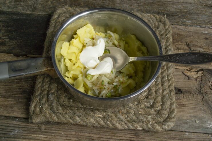 The secret to a creamy filling: Adding mayonnaise to the potato mixture. Mayonnaise being added to the potato and onion filling in a saucepan.