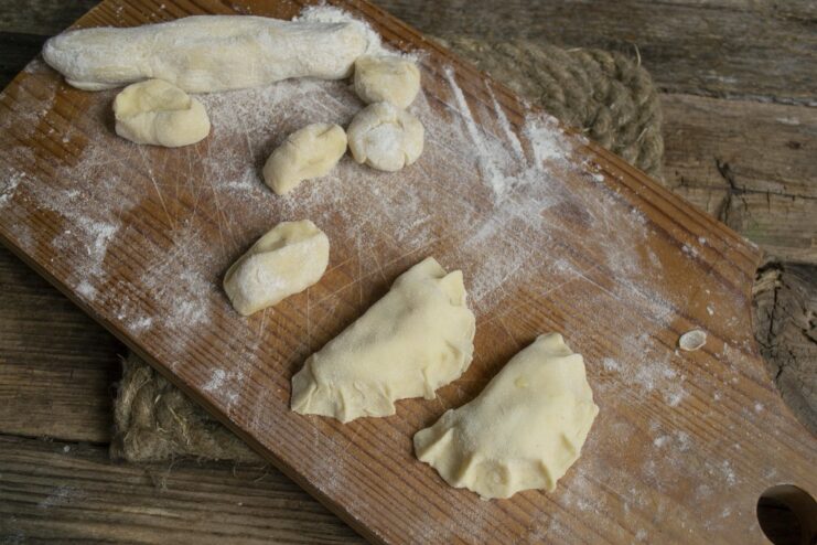 Carefully pinch the edges to seal the vareniki and create a beautiful shape. A hand pinching the edges of a varenik to seal the potato filling inside.