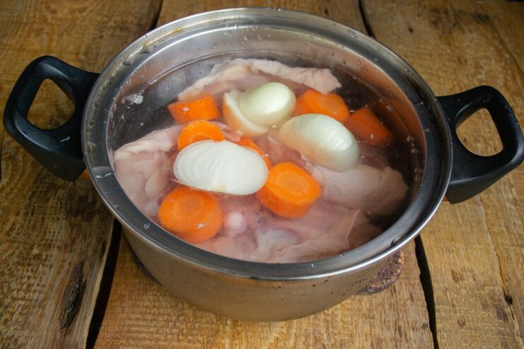 Step 1: Boiling the chicken with vegetables to create a flavorful broth. Chicken thighs and vegetables simmering in a pot of water to make broth.