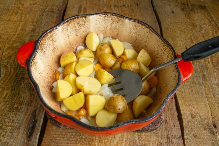 Step 4: Adding chopped new potatoes to the pot. Chopped new potatoes being added to the carrots and onions in the pot.