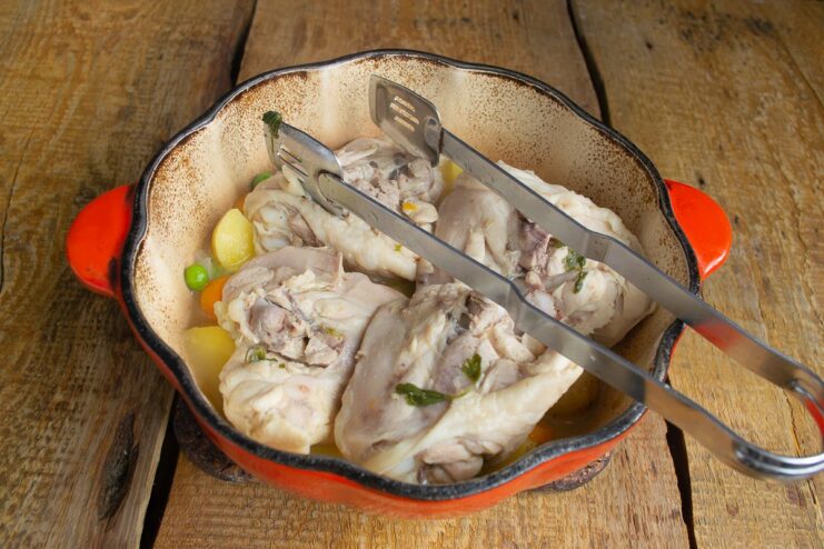 Step 6: Placing the cooked chicken pieces on top of the stewed vegetables. Pieces of boiled chicken being placed on top of the cooked vegetables in the pot.