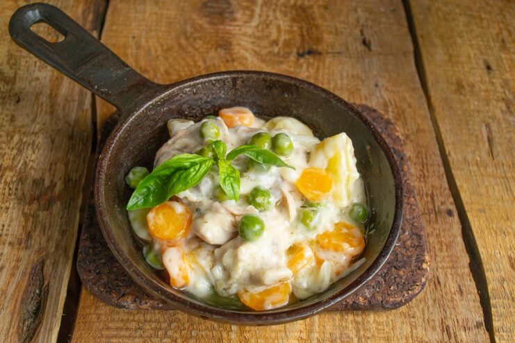 The finished dish, ready to be served and garnished with fresh herbs. The finished boiled chicken and vegetable stew in a pot, garnished with fresh basil.