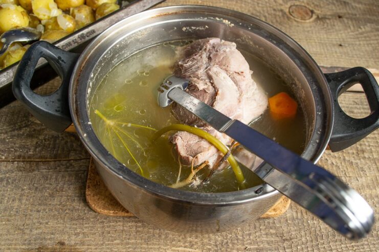 Preparing the tender meat and flavorful broth Coarsely chopped boiled pork on a cutting board next to a bowl of strained broth.