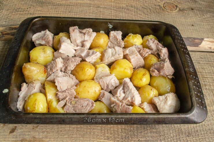 Combining the meat and potatoes for the bake Pieces of boiled pork being added to the potatoes and onions in the baking dish.