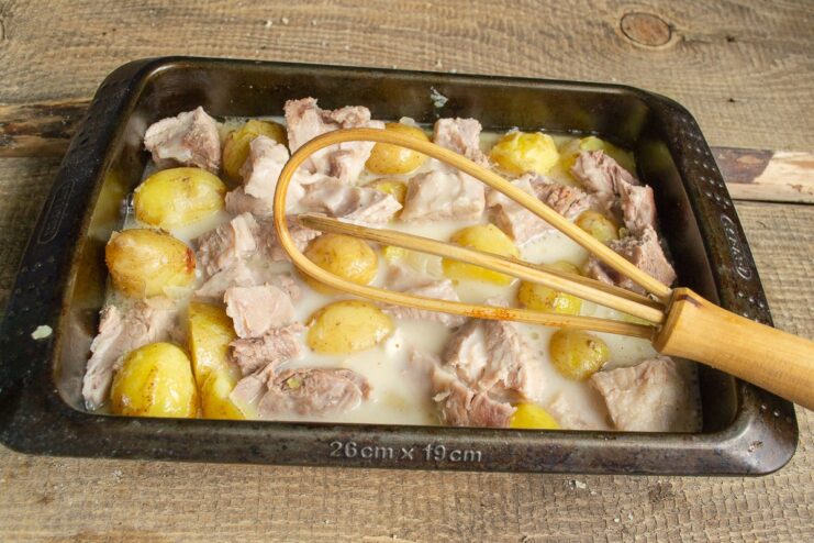 Covering the ingredients with the savory sauce Pouring the broth and flour sauce over the meat and potatoes in the baking dish.