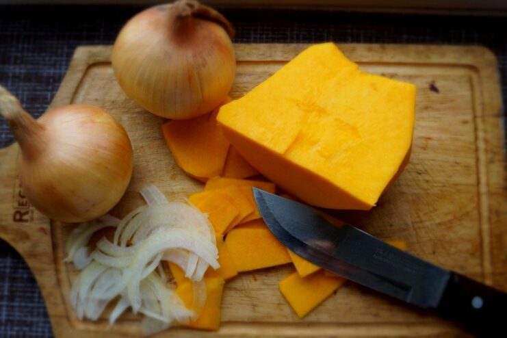 Preparing the vegetable filling for the lasagna A cutting board with thinly sliced pumpkin and finely chopped onions ready for cooking.