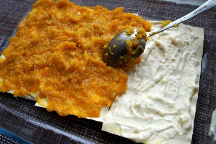 Adding the savory pumpkin filling to the lasagna A layer of cooked pumpkin and onion filling being spread over the Béchamel sauce in the lasagna.
