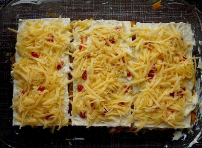 Finishing touch: Topping the lasagna with cheese before baking The final layer of lasagna topped with Béchamel sauce, grated cheese, and a decorative swirl of ketchup.