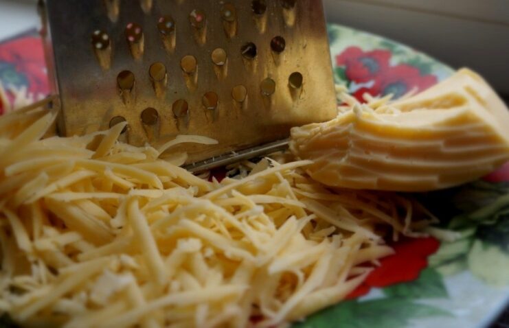 Grating cheese for the perfect lasagna topping A block of yellow cheese being grated on a coarse box grater into a small pile.