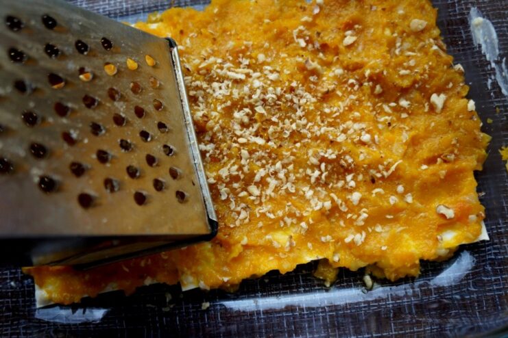 Adding a nutty crunch: Grating walnuts over the filling Walnuts being grated directly over a layer of lasagna filling in a baking dish.