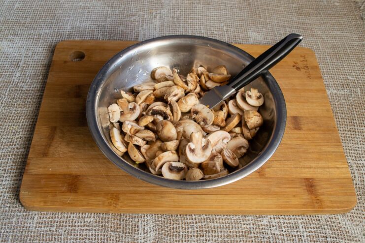 Thinly slicing fresh button mushrooms for the cabbage roll filling Close-up of hands slicing fresh button mushrooms on a cutting board.