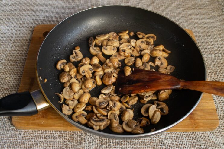 Sautéing sliced mushrooms in a pan until golden brown Sliced mushrooms being sautéed in a hot frying pan.