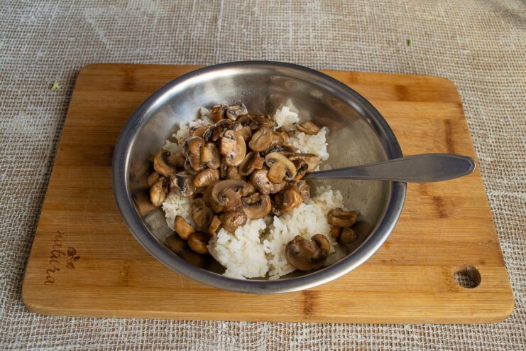 Combining cooked rice and sautéed mushrooms for the filling A bowl containing cooked rice with sautéed mushrooms being added.