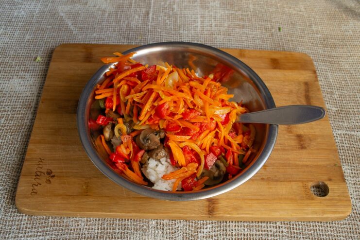 Mixing all filling ingredients: rice, mushrooms, and vegetables Sautéed vegetables being added to the rice and mushroom mixture in a bowl.