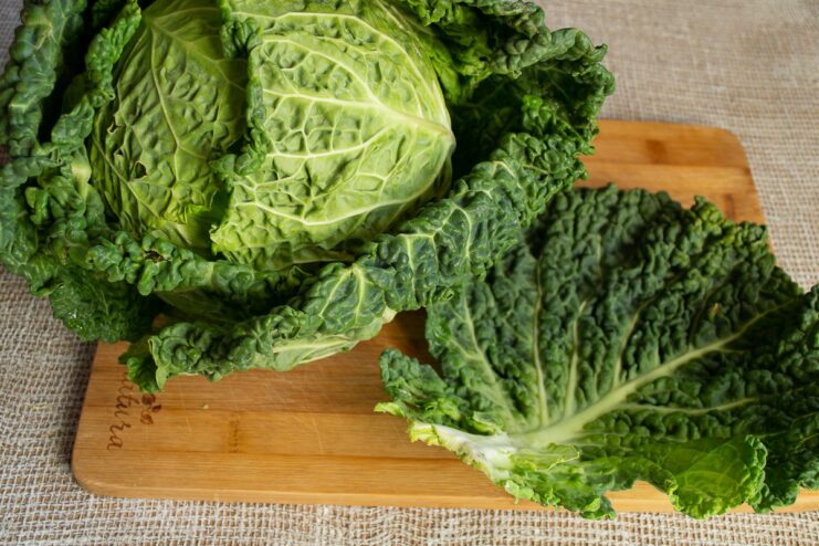 Pro tip: Always start by removing the outer, tougher leaves from your Savoy cabbage. A head of Savoy cabbage with the outer damaged leaves being removed by hand.