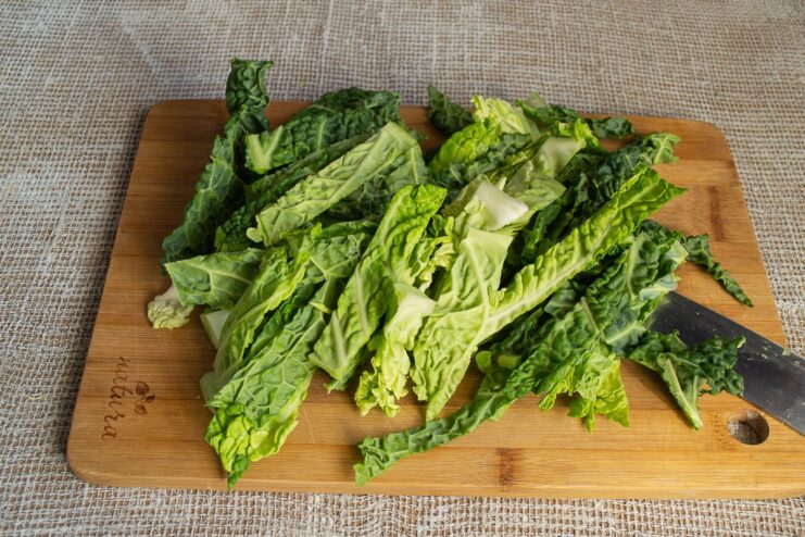Cutting Savoy cabbage into uniform strips for even cooking in the gratin. A pile of freshly sliced Savoy cabbage leaves on a cutting board.