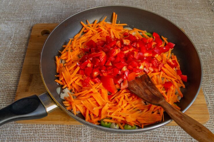 Sautéing onions, carrots, and peppers to build a flavorful base for the gratin filling. Chopped vegetables sautéing in a skillet to create the gratin's filling.