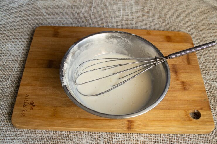 Creating a smooth, lump-free soy milk batter to bind the gratin layers. Whisking flour and soy milk in a bowl to make a smooth batter.