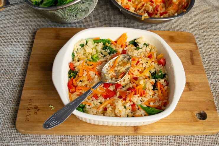 Adding a generous layer of the savory rice and vegetable filling. Spreading the rice and vegetable mixture over the cabbage layer in the baking dish.