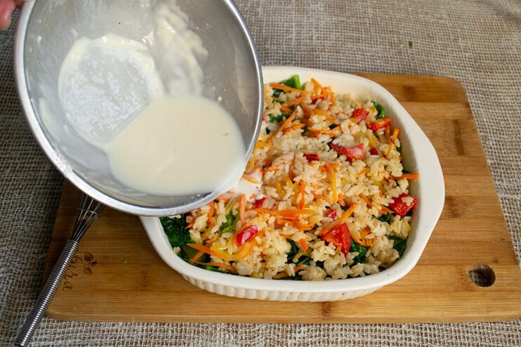 Finishing the layers and pouring the soy batter to bind everything together. Pouring the soy milk batter over the final layer of rice and vegetables in the gratin.
