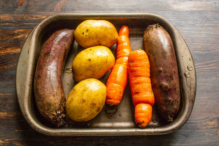 Baked beets, carrots, and potatoes on a baking sheet, ready for the salad. Baked whole beets, carrots, and potatoes cooling on a baking sheet.