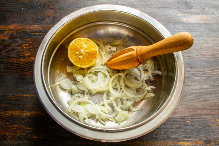 Slicing onion into thin half-rings for marinating. A hand slicing a red onion into thin half-rings on a cutting board.