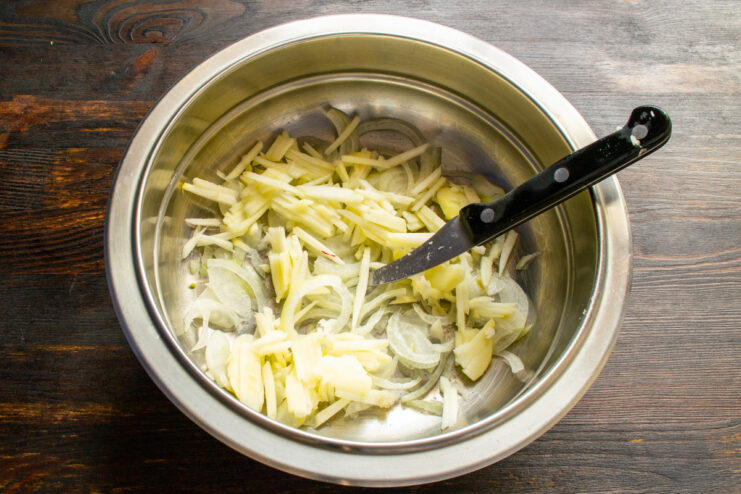 Mixing sliced apple with marinated onions to prevent browning. A bowl with sliced apples being mixed with marinated onions.
