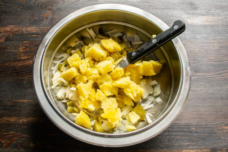 Adding diced baked potatoes to the salad bowl. Diced baked potatoes being added to a large bowl with other salad ingredients.