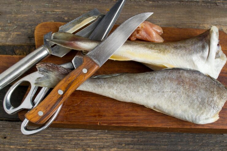 Step-by-step guide to cleaning and gutting navaga fish A person cleaning and gutting a whole navaga fish on a cutting board.