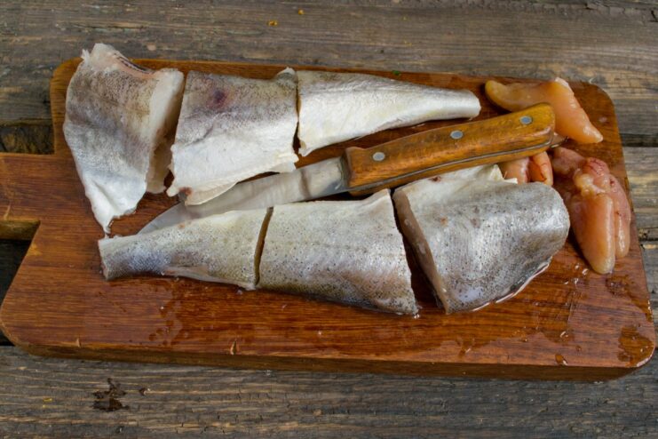 How to cut navaga fish into serving-sized portions Whole navaga fish being cut into several pieces on a wooden board.