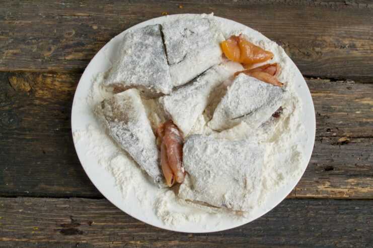 Coating navaga fish pieces in seasoned flour before frying Pieces of navaga fish being dredged in a plate of flour and salt.