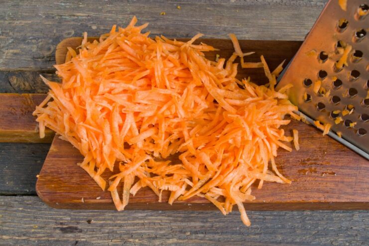 Grating fresh carrots for the fish marinade A hand grating a fresh carrot on a box grater for the marinade.
