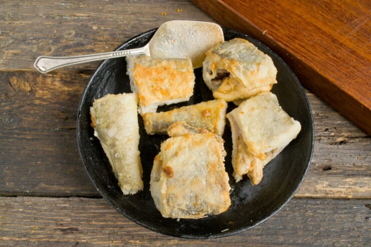 Pan-frying the flour-coated navaga until golden brown Pieces of flour-coated navaga fish being pan-fried to a golden brown crust.