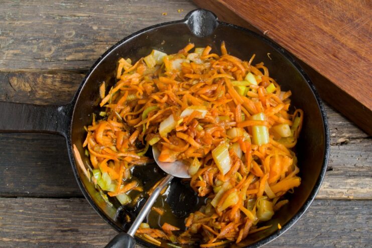 Sautéing carrots, leeks, and celery for the marinade base Sautéing chopped vegetables (carrots, leeks, celery) in a frying pan.