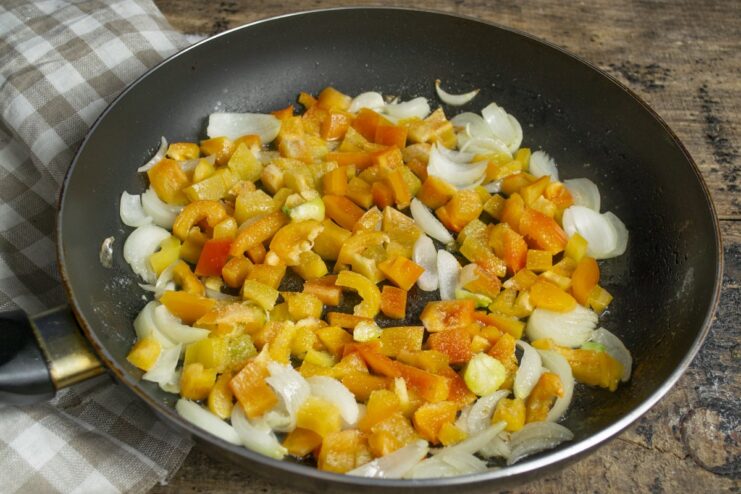 Sautéing Onions and Peppers for the Squid Stuffing Chopped onions and bell peppers being sautéed in a frying pan.