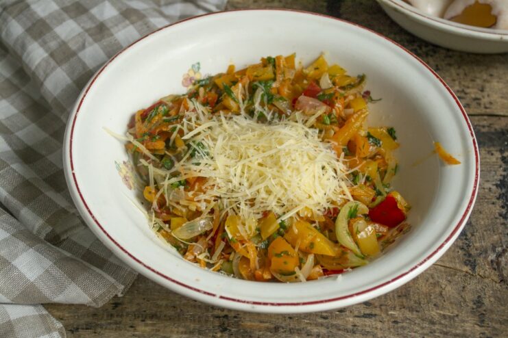 Combining the Cooked Vegetables with Grated Parmesan Cheese A bowl of cooked vegetable filling with grated Parmesan cheese being mixed in.