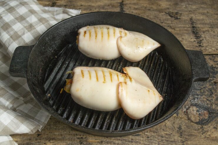 Grilling the Stuffed Squid to Perfection Stuffed squid tubes being placed on a hot grill pan to cook.