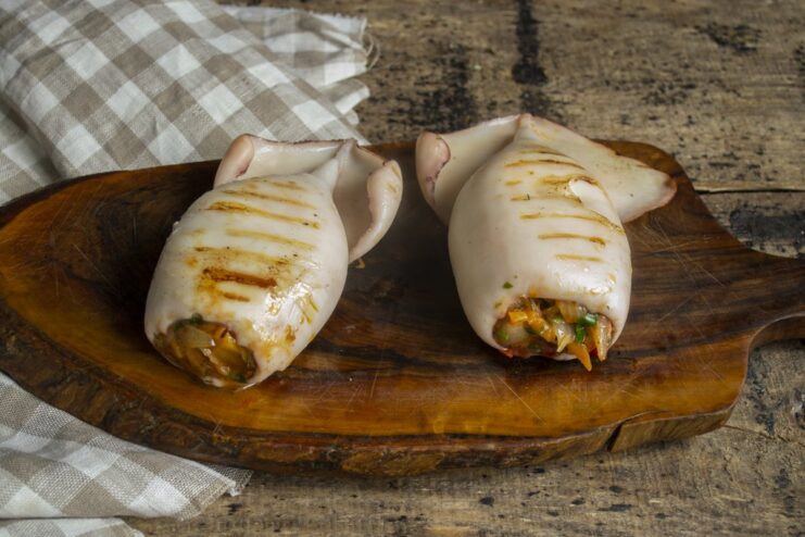 The Final Dish: Perfectly Grilled Stuffed Squid Ready to Serve A close-up of a cooked stuffed squid, sliced to show the vegetable and cheese filling.