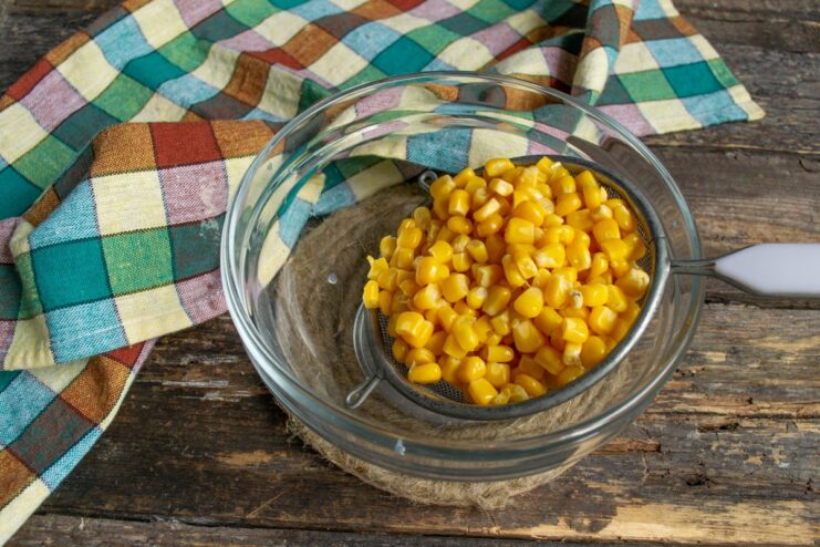 Preparing the Corn Kernels for the Pie Canned corn kernels being drained in a metal sieve over a bowl.