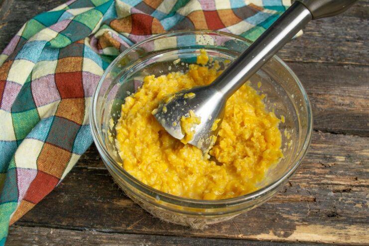 Blending Corn for a Moist Pie Batter A hand blender pureeing canned corn and liquid in a white bowl.