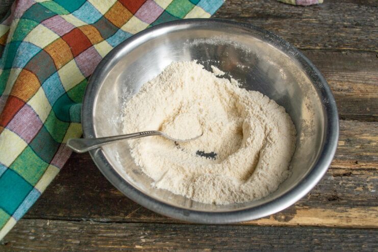 Combining Flour, Cornmeal, and Spices A white bowl containing a mix of flour, cornmeal, and paprika.