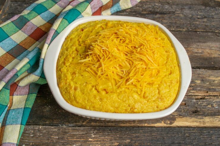 Topping the Corn Pie with Grated Cheddar Cheese The partially baked corn pie being generously sprinkled with grated cheddar cheese.