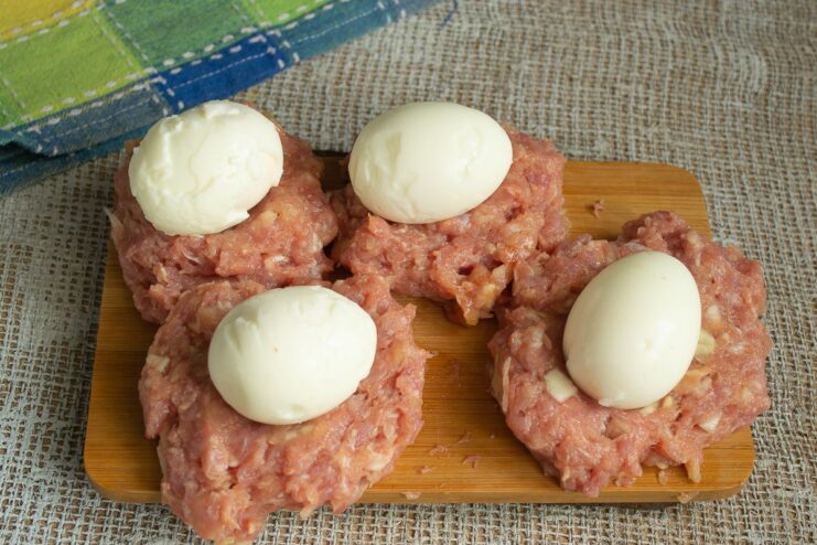 Wrapping the Soft-Boiled Egg in Pork Mince A peeled, soft-boiled egg being placed in the center of a flattened pork patty.