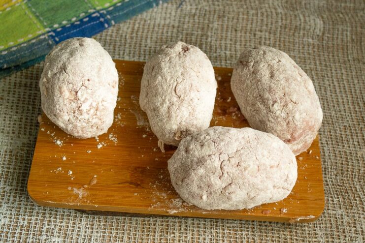 First Breading Step: Coating in Flour A raw Scotch egg being coated in a layer of all-purpose flour.