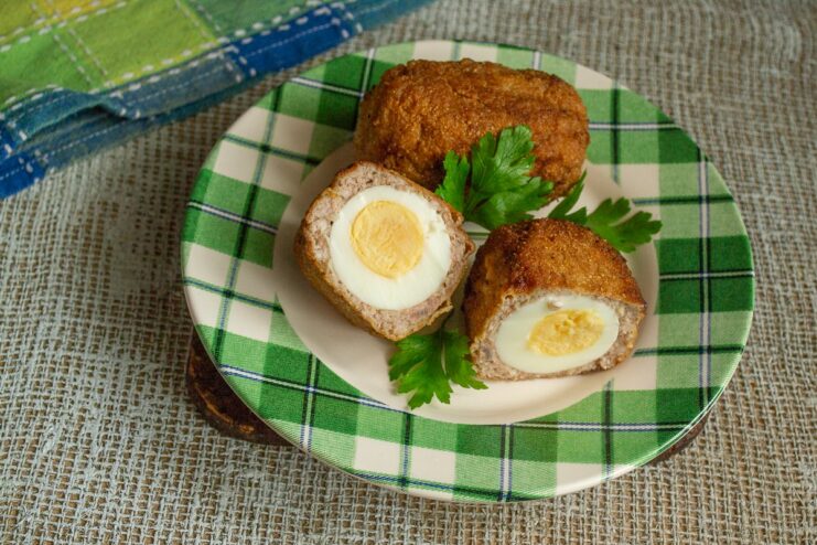 Serve Your Homemade Scotch Eggs Hot! Finished Scotch eggs on a plate, ready to be served, garnished with fresh herbs.