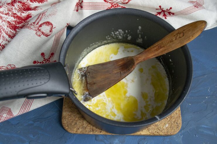 Simmering the cream sauce to thicken it and develop flavors. Creamy sauce simmering in a saucepan, being stirred with a whisk.
