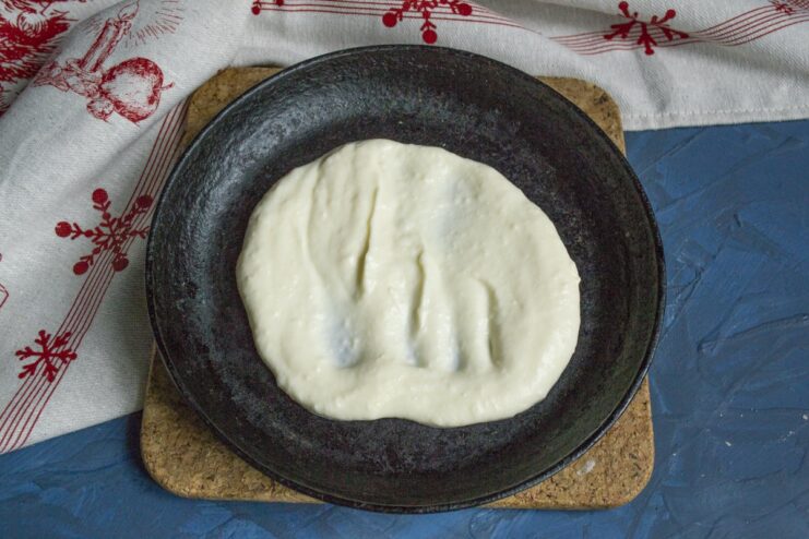 Layering the creamy sauce in an individual skillet before adding the fish. Pouring the creamy white sauce into a small, individual baking skillet.
